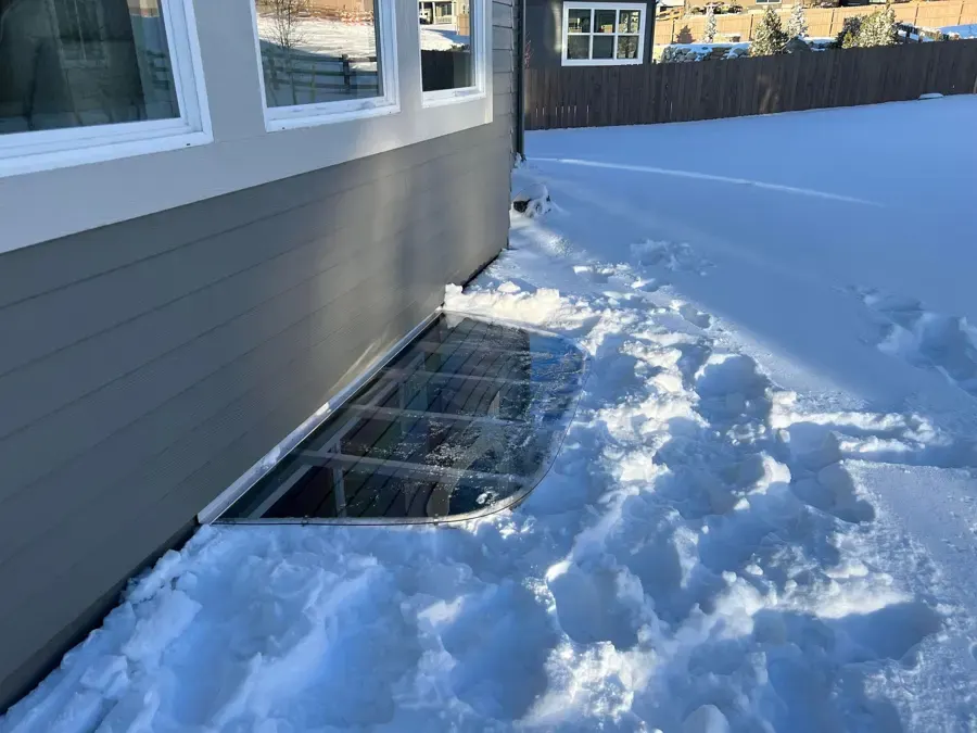 Snow piled against a basement window well cover at an Aurora home